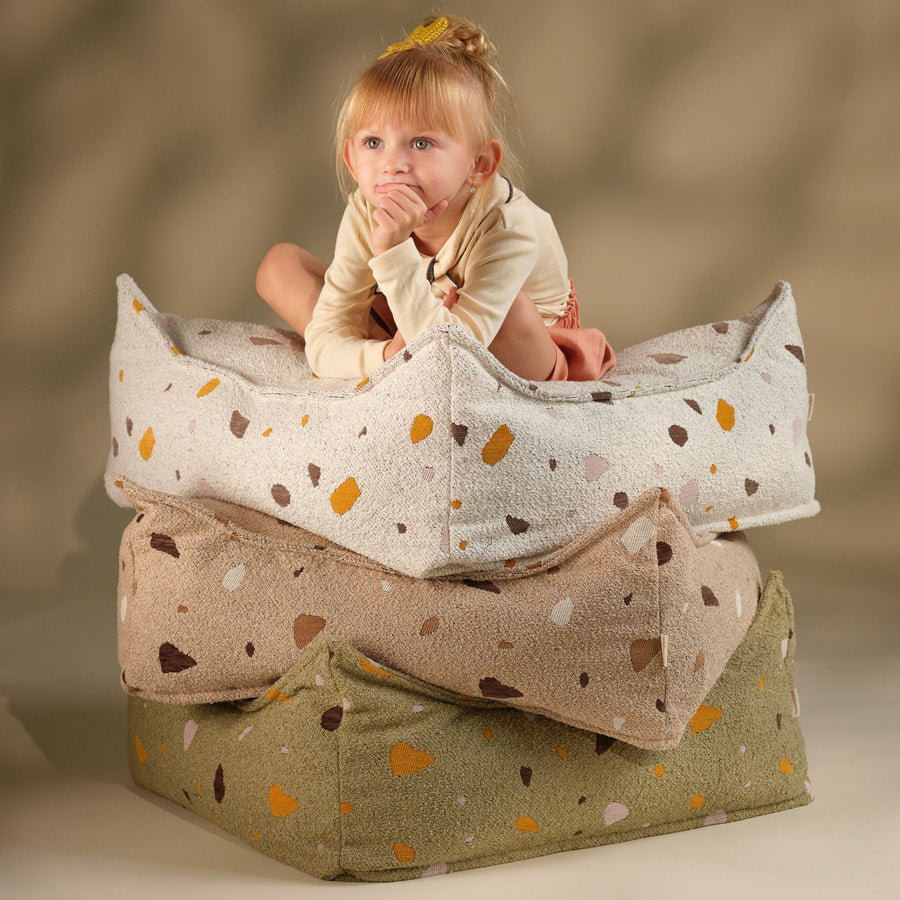 Kind sitzt auf den drei Ottomans von Wigiwama. Es gibt den Sitzsack für Kinder in den Farben Marble, Sand und Moos.