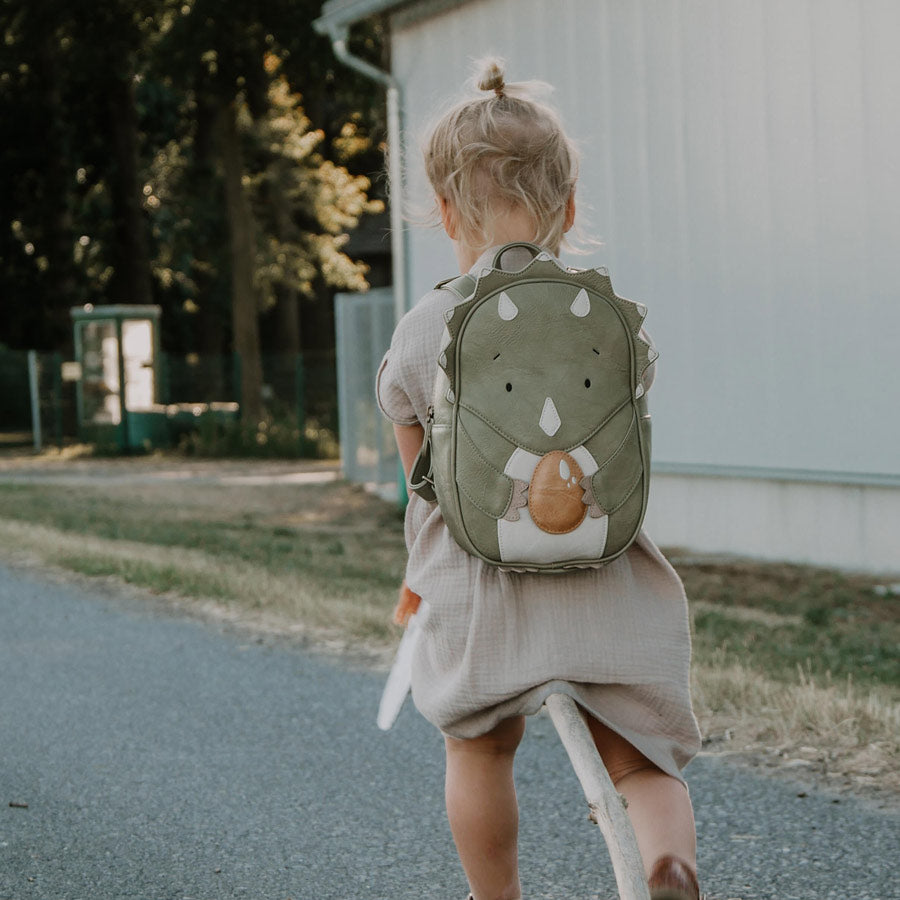 Mädchen trägt den Dino-Rucksack draußen und macht einen Ausflug