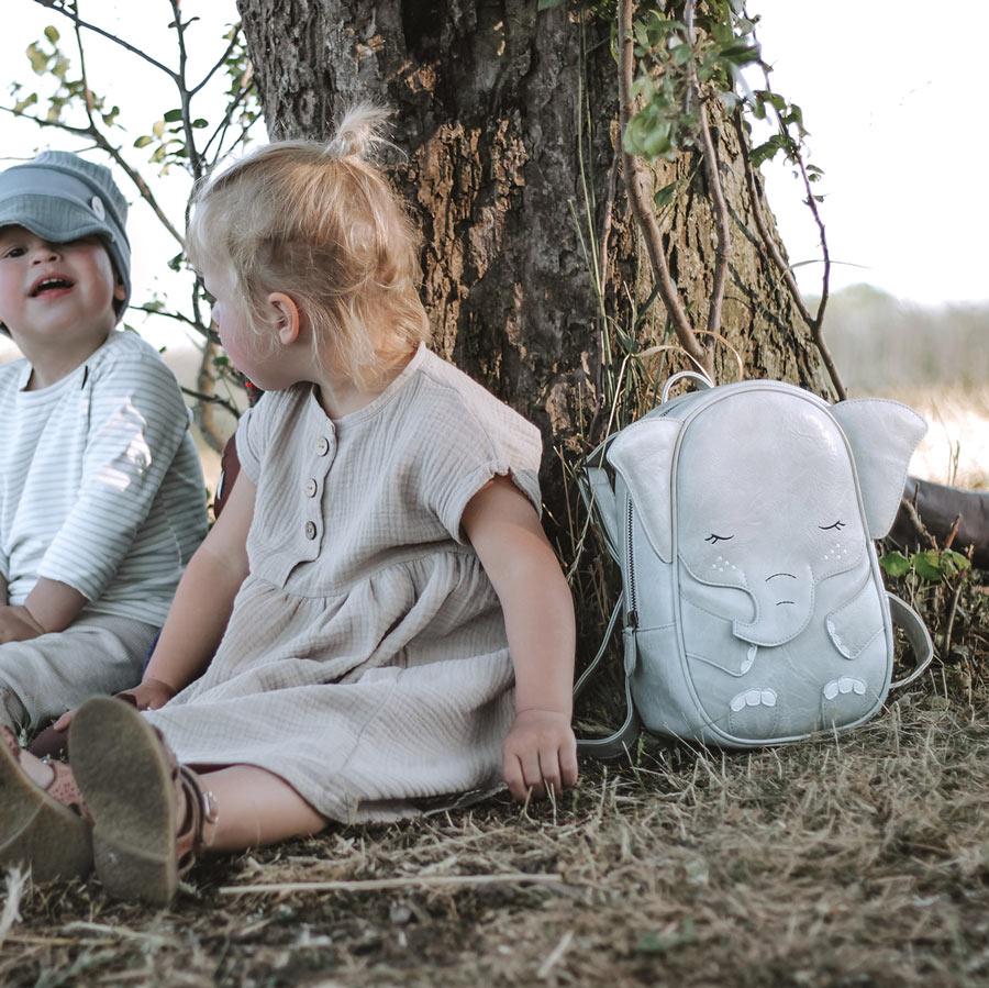 Zwei Kinder sitzen draußen und haben den Rucksack Elefant neben sich