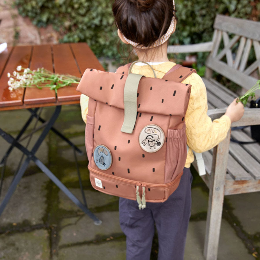 Der Rolltop Rucksack für Kinder in der Farbe Karamell hat schwarze Punkte und süße Patches zum Wechseln.
