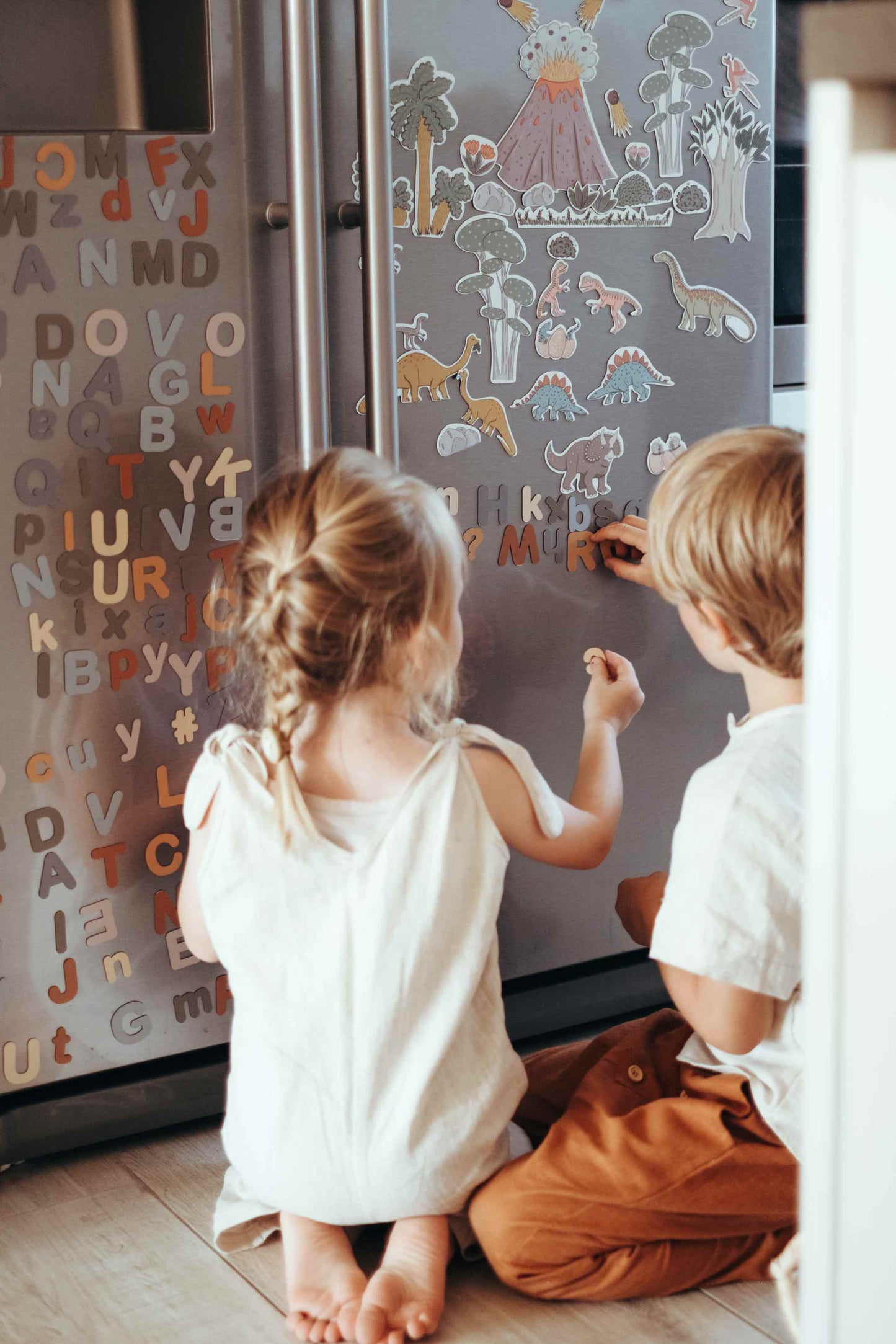 Zwei Kinder spielen am Kühlschrank mit den Magneten Buchstaben und Dinosaurier