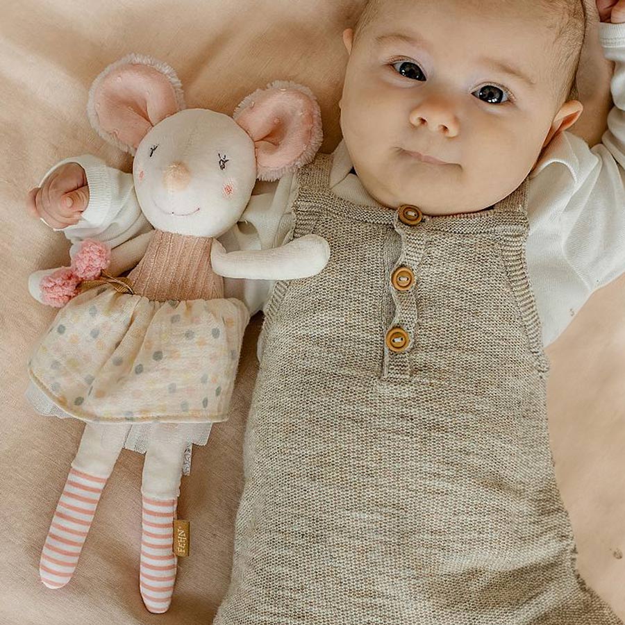 Baby liegt mit der Kuschelpuppe Maus im Arm auf einer Decke.
