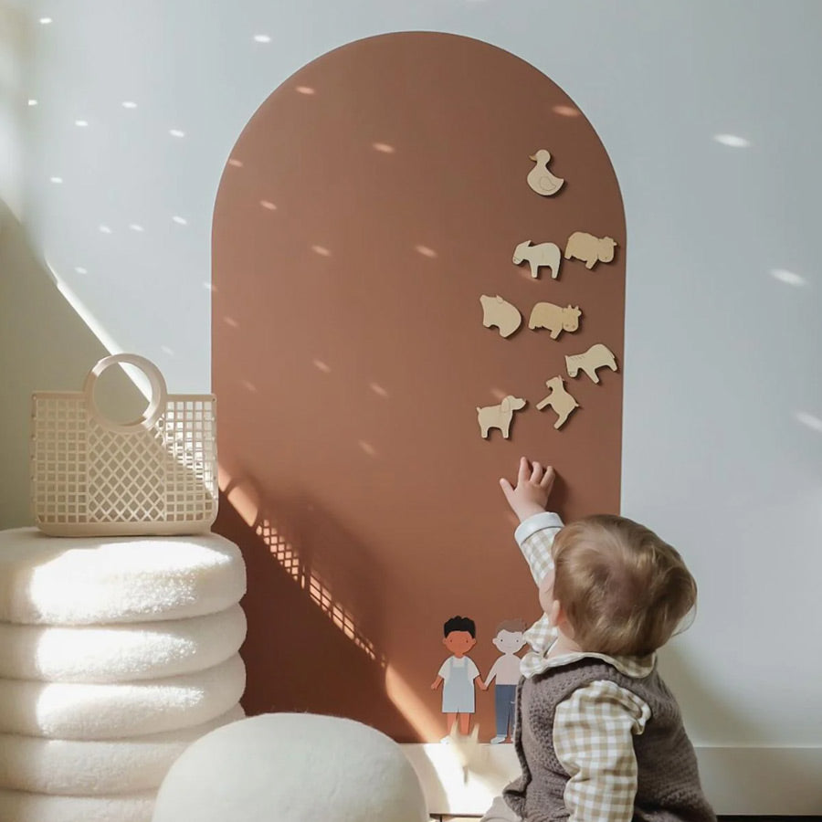 Kind spielt mit den Holzmagneten Bauernhof an der Magnettafel in der Farbe Karamell.
