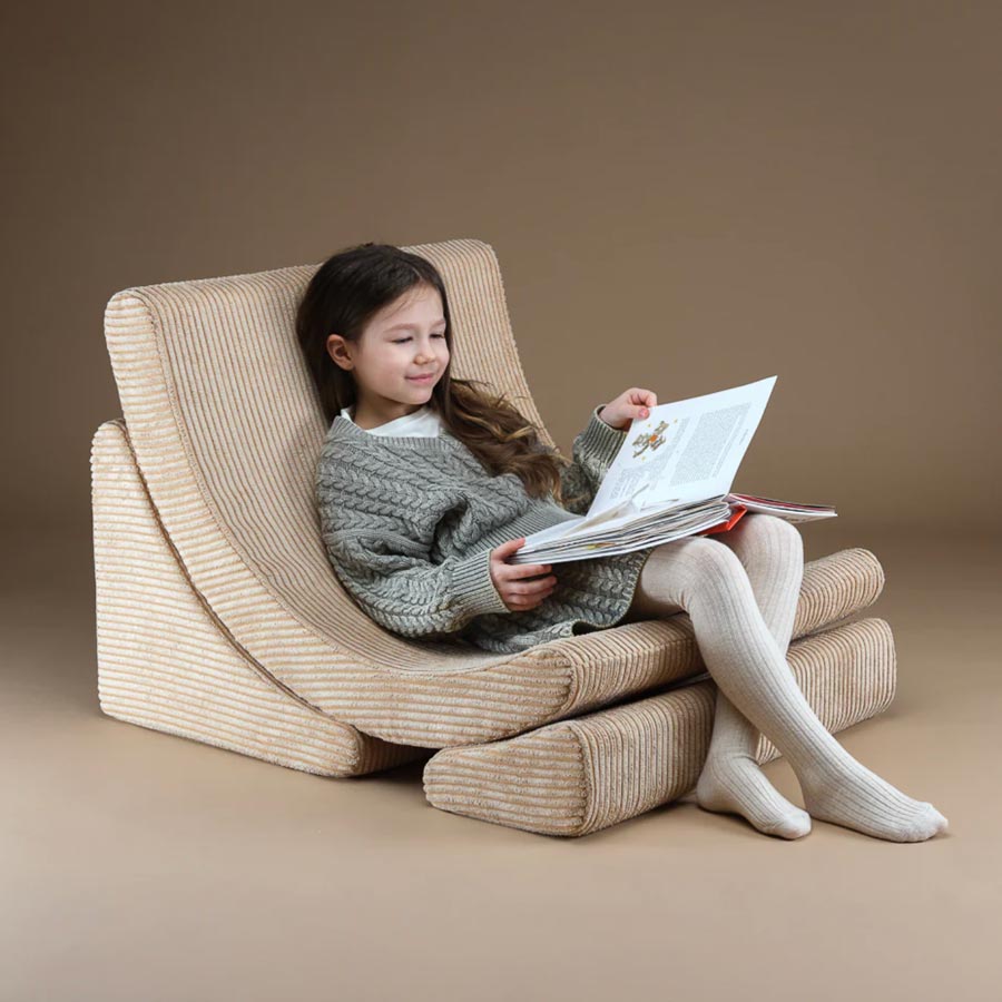 Schulkind sitzt auf dem Moon Chair in der Farbe Beige und liest ein Buch.