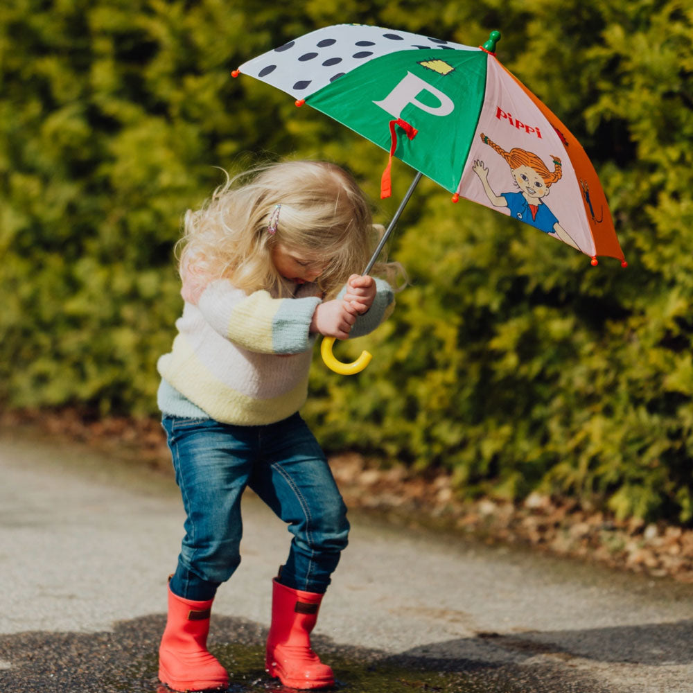 Kind springt in eine Pfütze und hält dabei den lustigen Regenschirm von Pippi Langstrumpf.