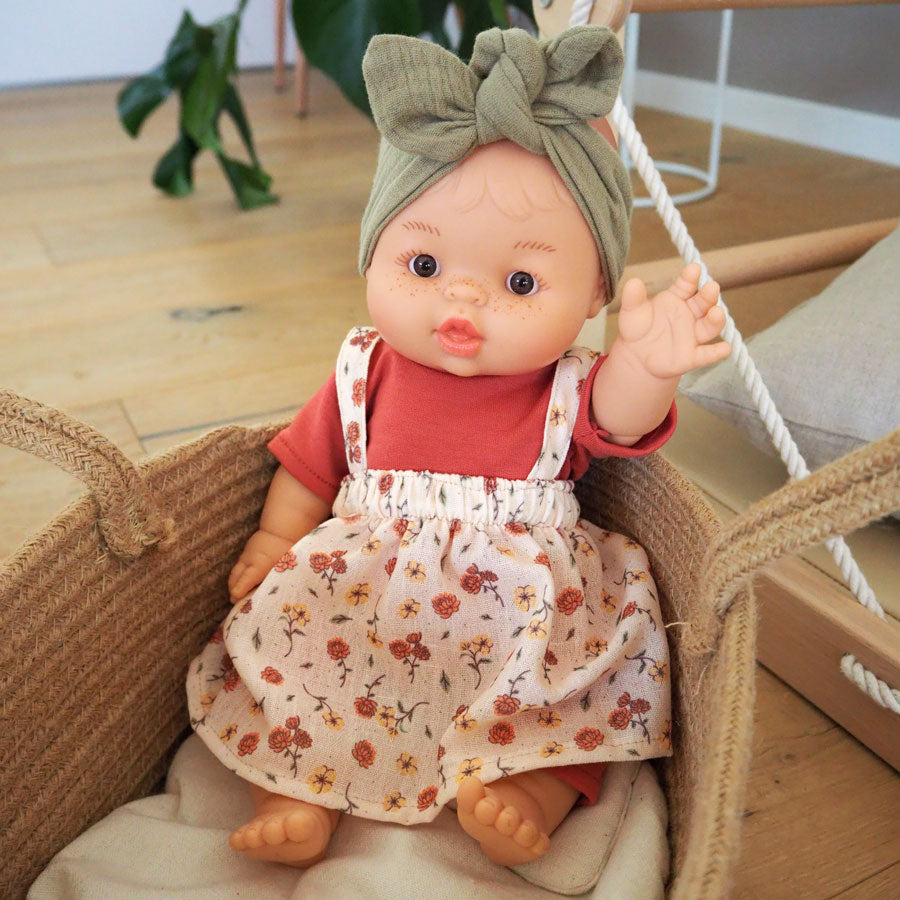 Die Puppe Gordi trägt ein oliv-grünes Stirnband und ein farbenfrohes Outfit