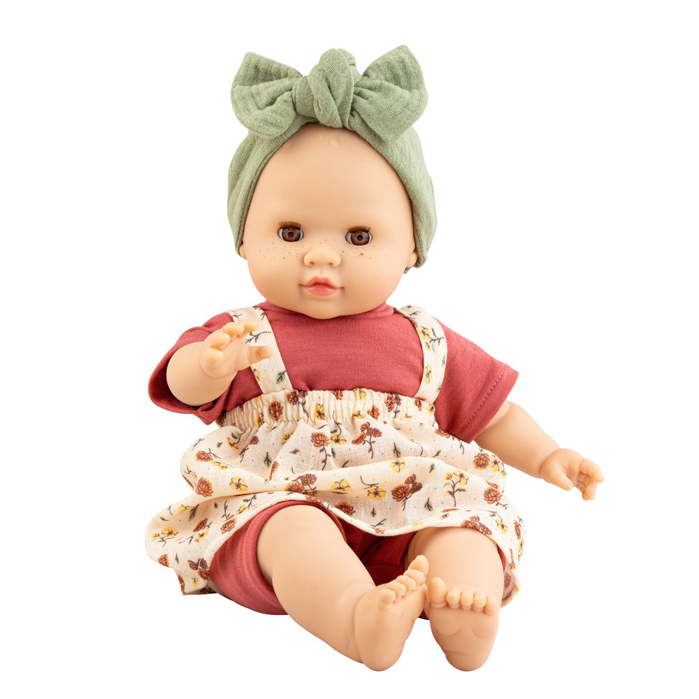 Die Puppe Julia hat helle Haut, braune Augen und leichte Sommersprossen. Sie trägt ein hübsches Puppenoutfit mit Kleidchen, Shirt, kurzer Hose und Stirnband.