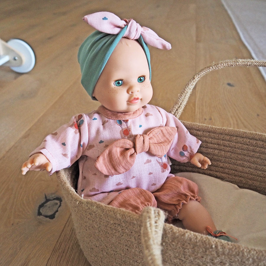 Spielzeugpuppe von Paola Reina für Kinder sitzt im Puppentragekorb