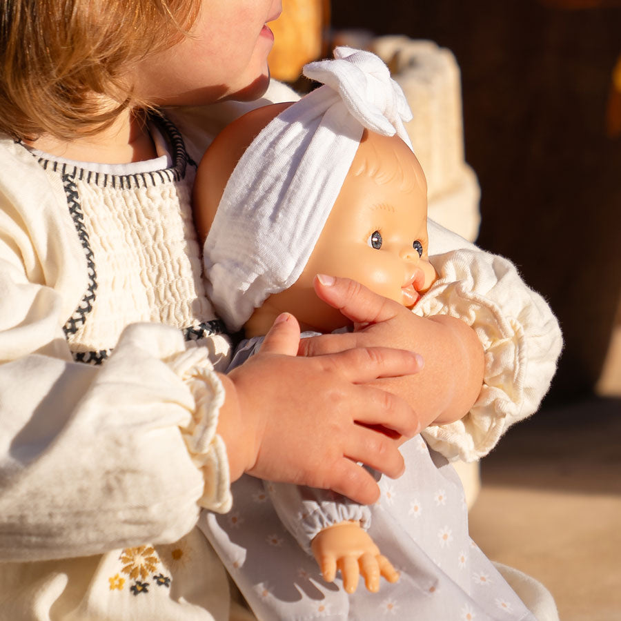 Mädchen hält die Babypuppe Raky im Arm und spielt draußen in der Sonne mit ihr.