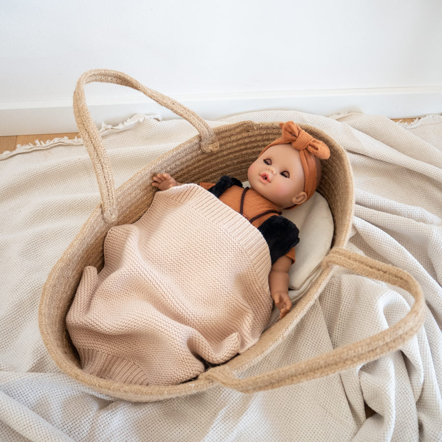 Der Puppentragekorb kommt mit einer Matratze und einem Kissen in offwhite/beige und einer gehäkelten Decke in einem beige/rose Ton.