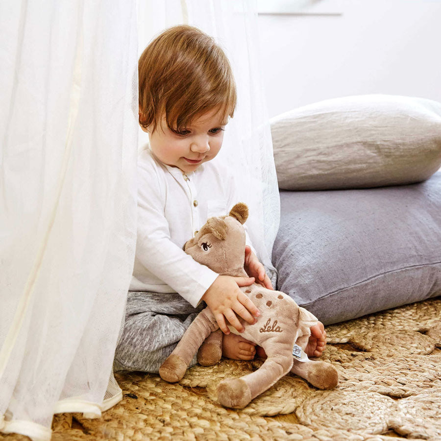 Kleinkind spielt mit dem Kuscheltier Rehkitz Lela von der Marke Lässig