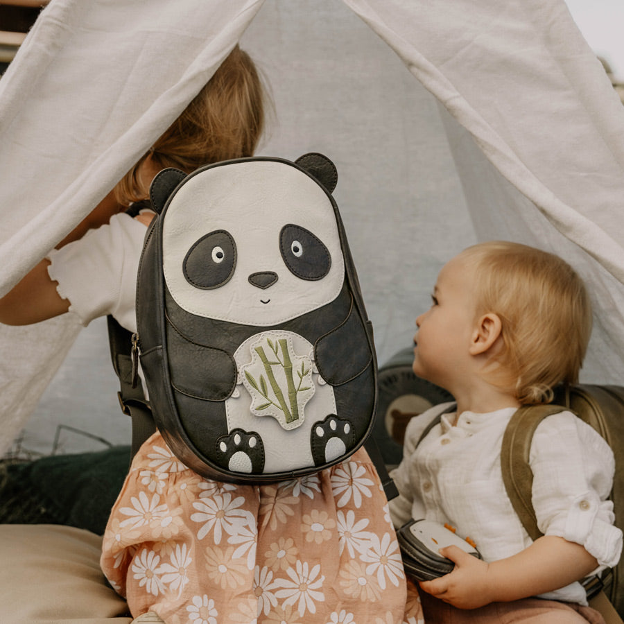 Mädchen spielt draußen in einem Zelt und hat den Panda-Rucksack von Little Who auf dem Rücken