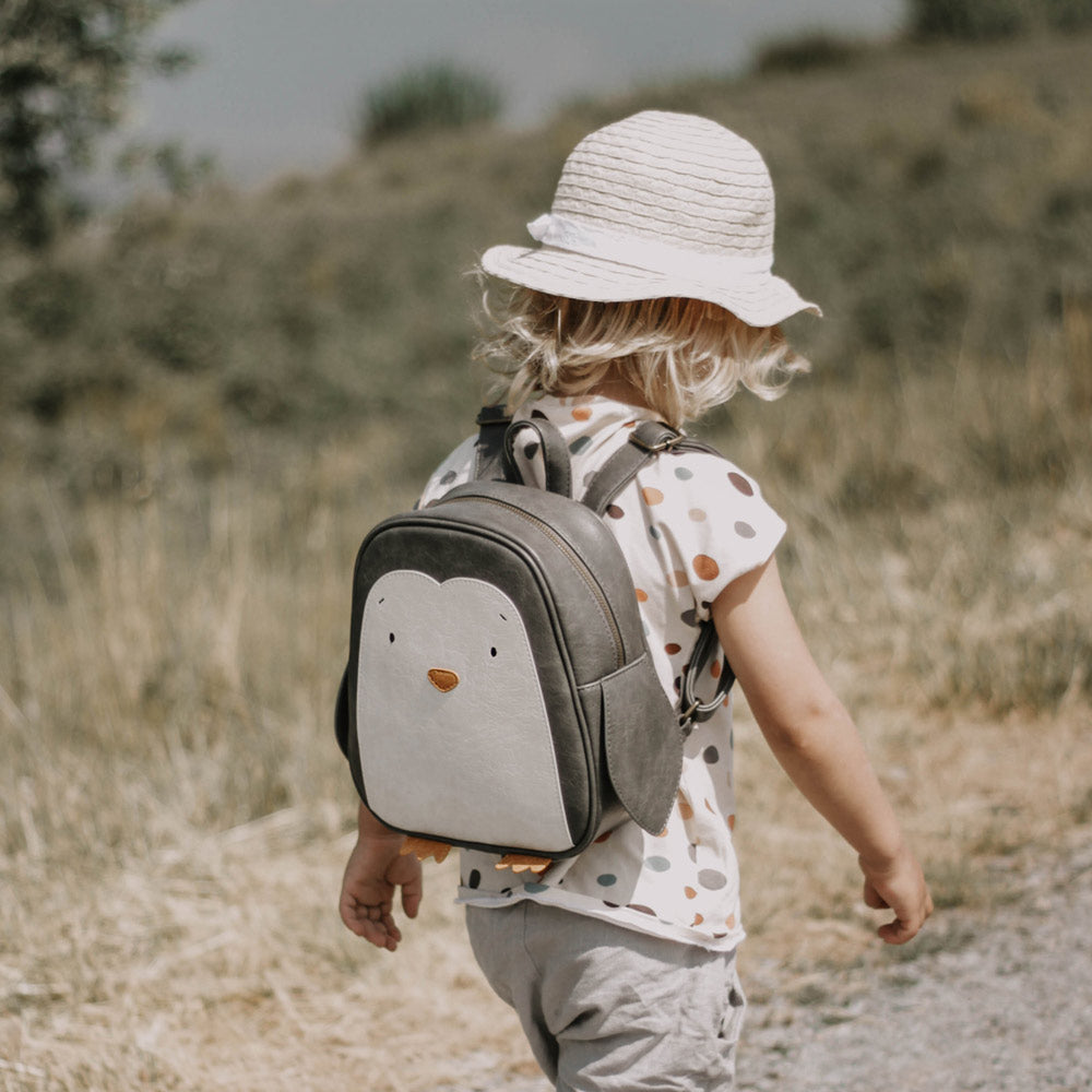 Kind trägt den Pinguin-Rucksack in der Farbe schwarz/grau und weiß mit einer orangenen Nase und Füßen.