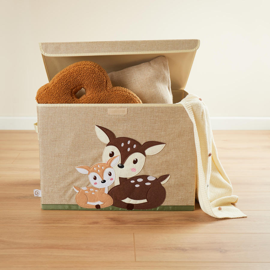 Die Aufbewahrungsbox ist rechteckig, ist in der Farbe Natur / beige und hat zwei Rehe aus Filz auf der Vorderseite. Es ist ein großes Reh und ein kleines Rehkitz, die miteinander kuscheln. Die Rehe sind in der Farbe hell- und dunkelbraun. In der Box liegen zwei Kissen und ein Mulltuch.