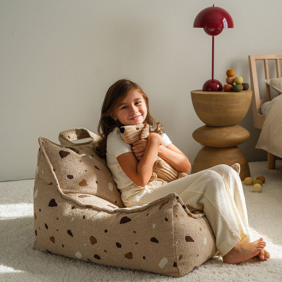 Mädchen sitzt auf dem Sitzsack von Wigiwama in der Farbe beige und kuschelt mit einem Kuscheltier.