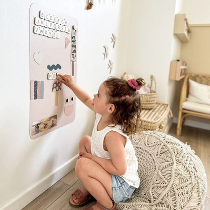 Mädchen spielt an einer rosa-beige-farbenden Magnetwand mit Buchstabenmagneten aus Holz und geometrischen Magneten