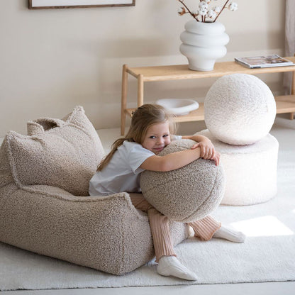 Mädchen sitzt auf dem Kindersessel von Wigiwama in der Farbe beige.