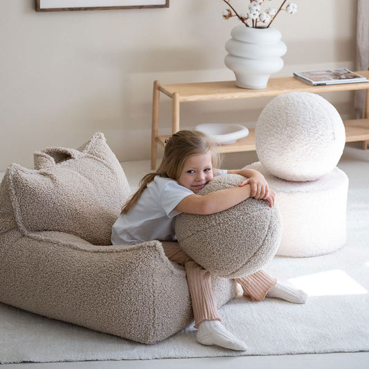 Mädchen sitzt auf dem Kindersessel von Wigiwama in der Farbe beige.