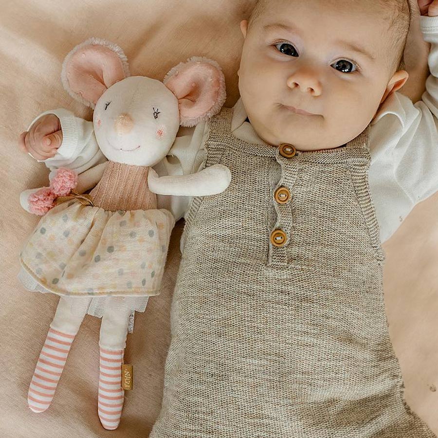 Baby liegt mit der Kuschelpuppe Maus im Arm auf einer Decke. 