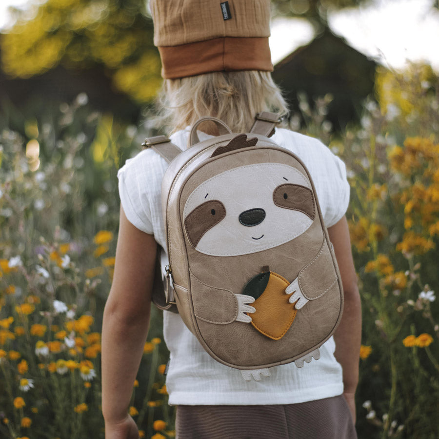 Kind macht einen Ausflug und trägt den Faultier-Rucksack in einem hellen braun und einer gelben Zitrone in den Händen