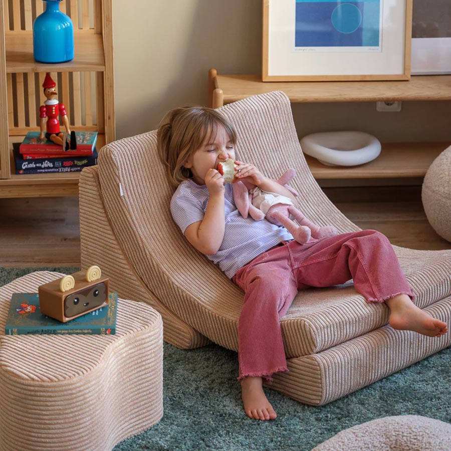 Kind sitzt auf dem Moon Chair in der Farbe Beige und isst einen Apfel. Der Sessel steht im Wohnzimmer und passt durch die schlichte Farbe perfekt in den Raum. 