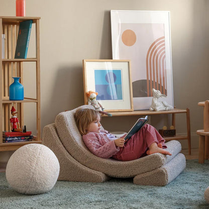 Mädchen sitzt im Wohnzimmer auf dem Moon Chair Sessel in der Farbe beige und liest ein Buch. Der Sessel passt farblich perfekt ind en Raum. 