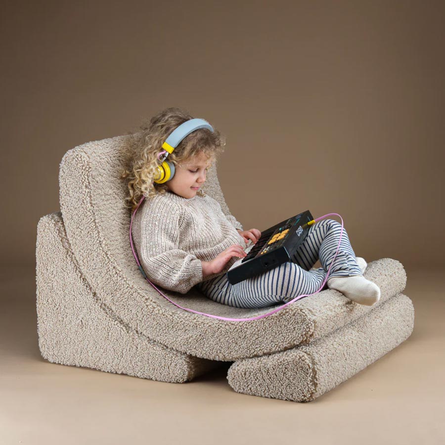 Mädchen sitzt entspannt mit ihrem Keyboard und ihren Kopfhörern auf dem Moon Chair Sessel in der Farbe beige. 