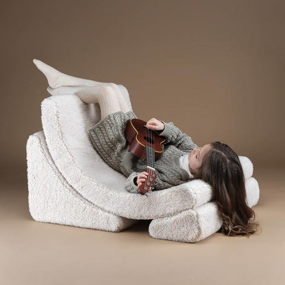 Mädchen liegt mit einer kleinen Gitarre auf dem Moon Chair Sessel in der Farbe Creme. Sie liegt mit den Beinen nach oben und mit dem Kopf nach unten. Auch diese Position ist für die Kids gemütlich. 