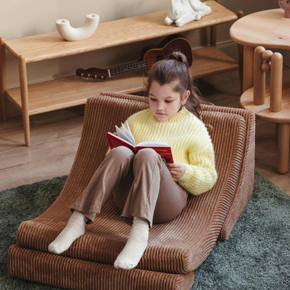 Schulkind sitzt auf dem Moon Chair in der Farbe Toffee und liest entspannt ein Buch. Der Sessel steht in einem Raum und passt durch die Farbe perfekt in den Raum. 