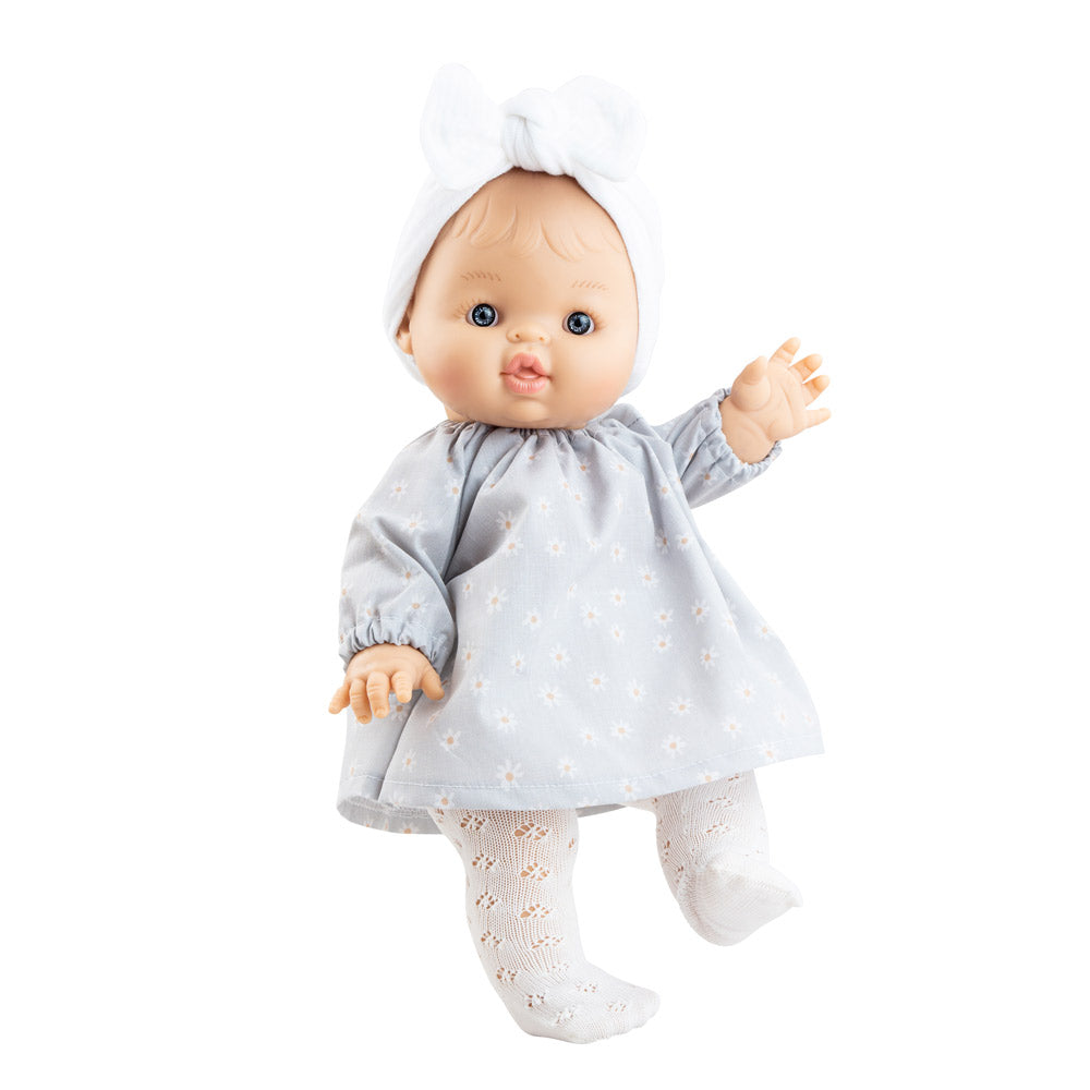 Puppe Raky hat blaue feststehende Augen, einen festen Körper und trägt ein hellblaues Puppenkleid mit Gänseblümchen und einer weißes Strumpfhose. 