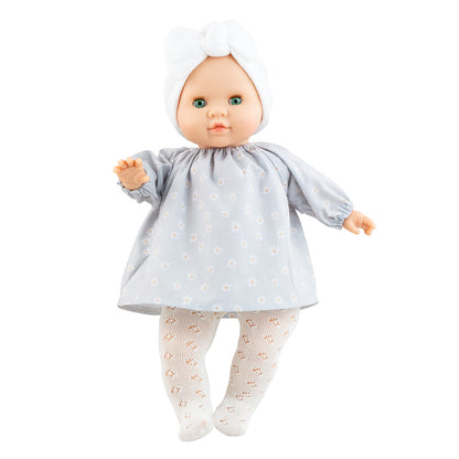 Die Puppe Ana hat grüne Augen, Sommersprossen und trägt ein hellblaues Kleid mit kleinen Gänseblümchen, sowie einer weißen Strumpfhose und einem weißen Stirnband. 