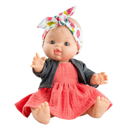 Die Puppe von Paola Reina hat helle Hau und blaue Augen. Die Spielzeugpuppe für Kinder trägt ein rotes Musselinkleid und eine graue Jeansjacke. Ihr Schleifenstirnband hat Kirschen und Blätter drauf.