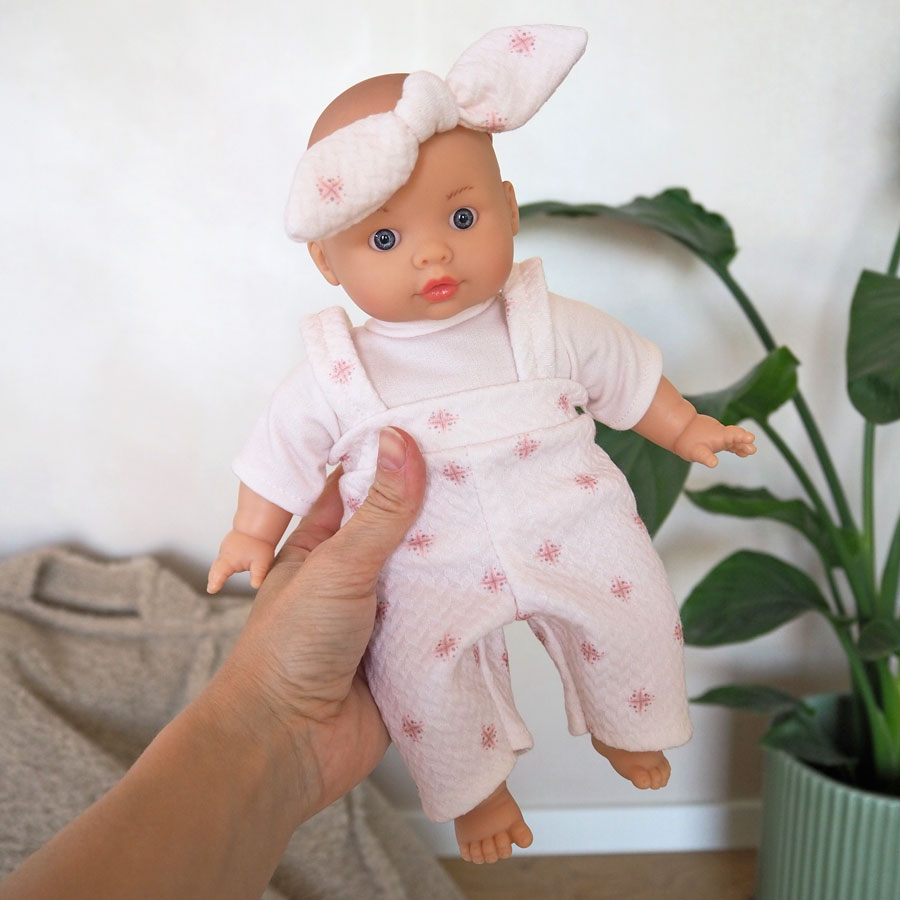 Die Puppe trägt ein rosa Shirt und eine rosafarbene Latzhose mit kleinen Muster