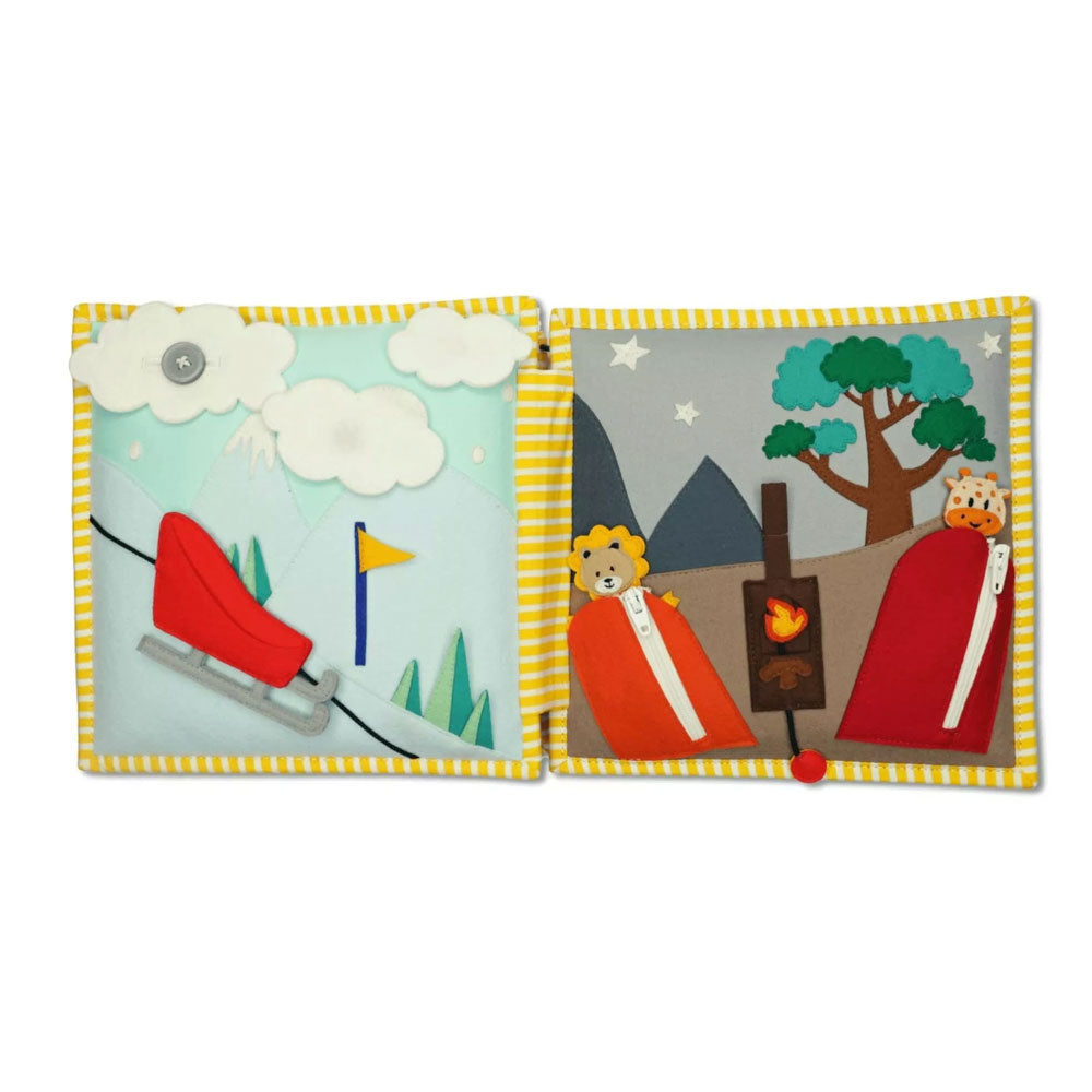 Schlitten, den die Kinder an einer Schnur den Berg runterfahren können. Die Wolke ist mit einem Knopf befestigt, mit dem die Kinder ihre Feinmotorik üben können. Auf der rechten Seite sind ein Löwe und eine Giraffe in jeweils einem Schlafsack zu sehen. Die Schlafsäcke kann man mit einem Reisverschluss öffnen. In der Mitte ist ein Lagerfeuer, das man mit einer Schnur an- und ausmachen kann. 