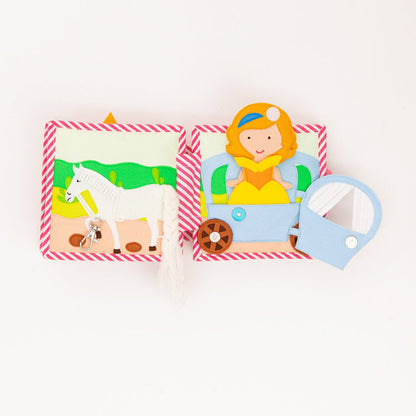 Zwei Seiten des Quiet Books mit einem Pferd , dass einen Karabinerhaken hat und eine Kutsche mit einer Prinzessin zieht. Die Tür von der Kutsche kann man öffnen. 