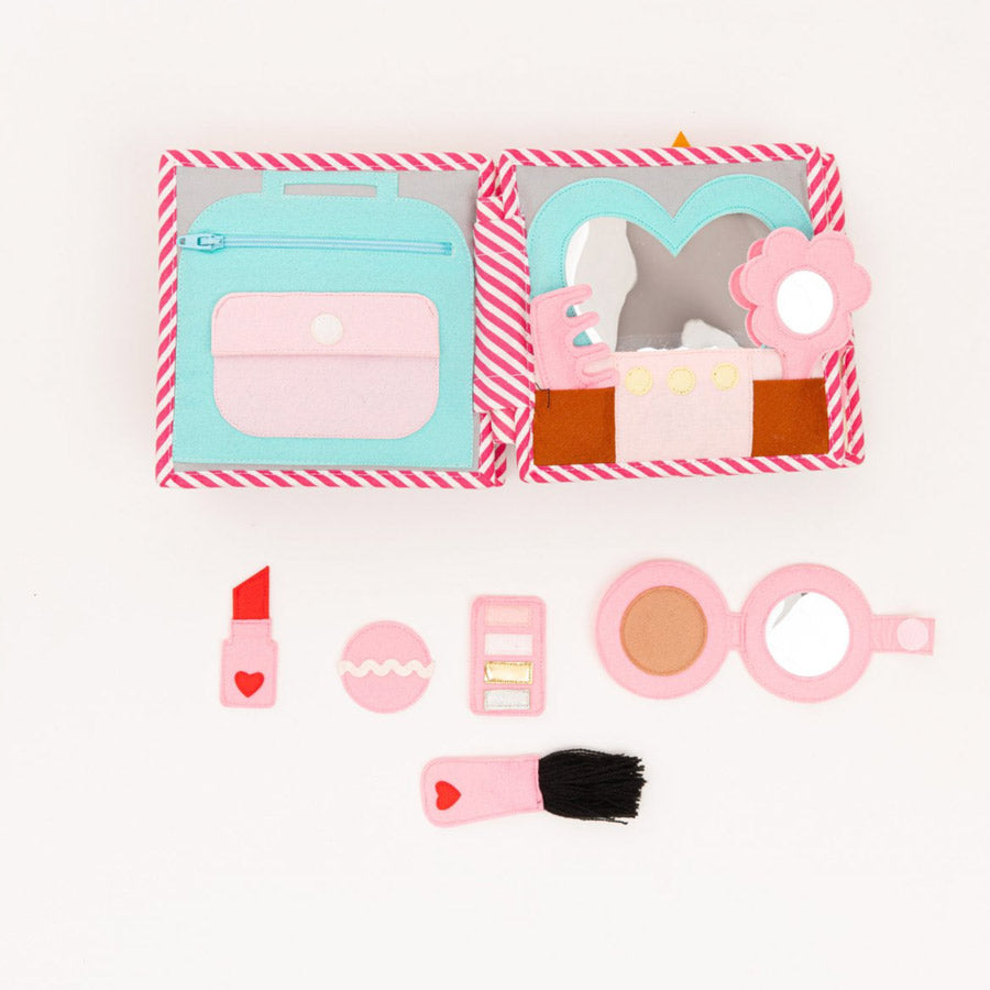 Auf einer Seite des Quiet-Books befindet sich eine Make-Up-Tasche, ein Spiegel und verschiedene Accessoires aus Filz, wie Lippenstift, Rouge und Pinsel.