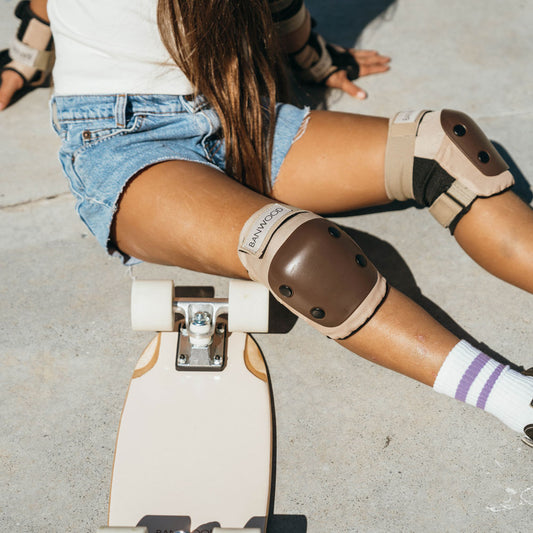 Mädchen mit Skateboard trägt die Knieschoner von Banwood. Die Knieschoner haben die Farbe beige mit braunen Schutzkappen. 