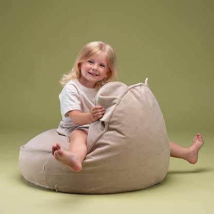 Mädchen sitzt spielerisch auf dem Sitzsack von Wigiwama in der Farbe beige. 