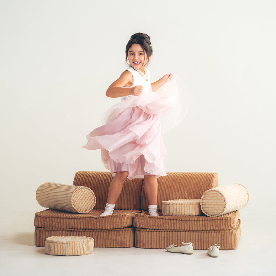 Schulkind tanzt mit einem festlichen Kleid auf dem Spielsofa für Kinder von der Marke Wigiwama