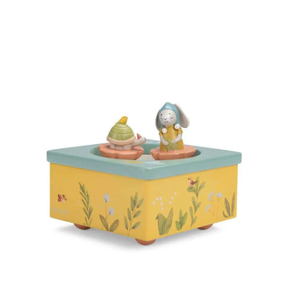 Die Spieluhr ist gelb mit einem blauen Rand und zwei Figuren drauf, nämlich eine Schildkröte und ein Hase.