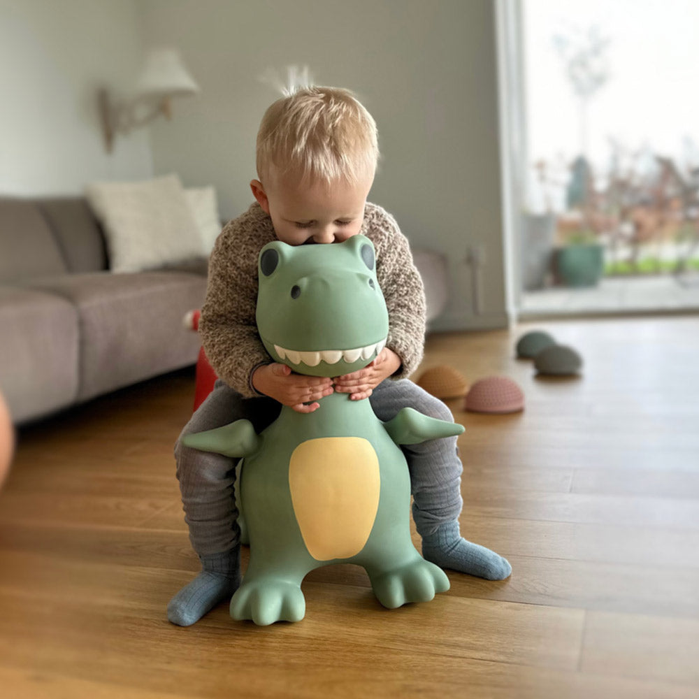 Kind springt freudig auf dem Hüpftier Dino in der Wohnung rum und freut sich