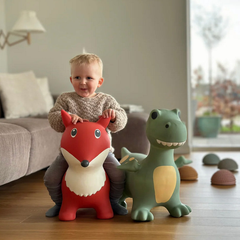 Ein Junge sitzt im Wohnzimmer auf dem Springtier Fuchs und neben ihm steht das Hüpfttier Dino in grün