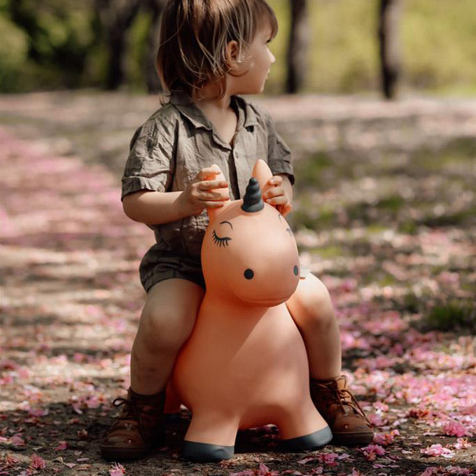 Kind spielt und hüpft auf dem Springtier Einhorn draußen in der Natur.