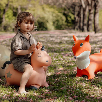 Kind sitzt auf dem Springtier Einhorn und springt damit auf einer Wiese umher, neben dem Hüpftier Fuchs